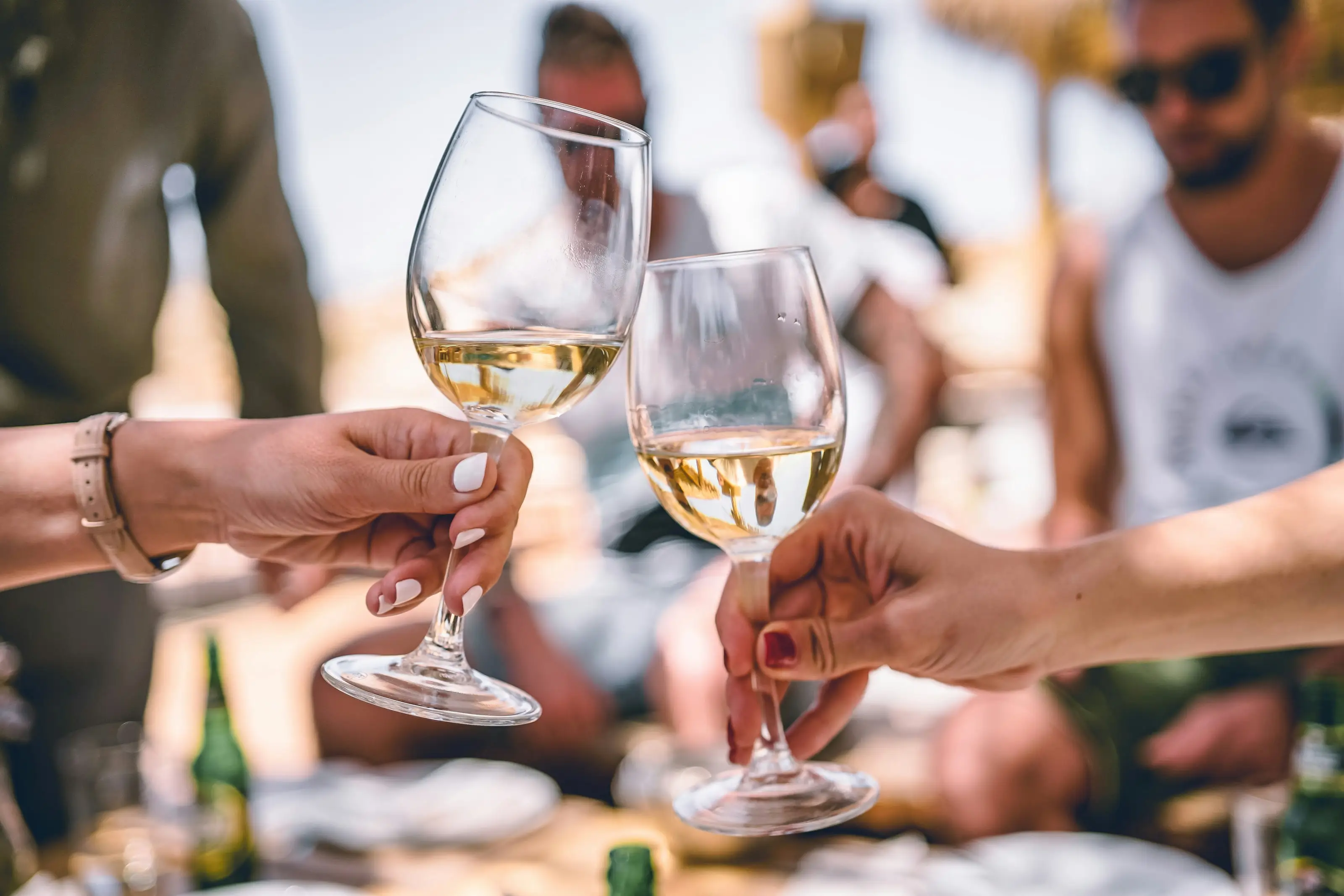 Mehrere Gläser Weißwein stoßen bei einer Feier im Freien an