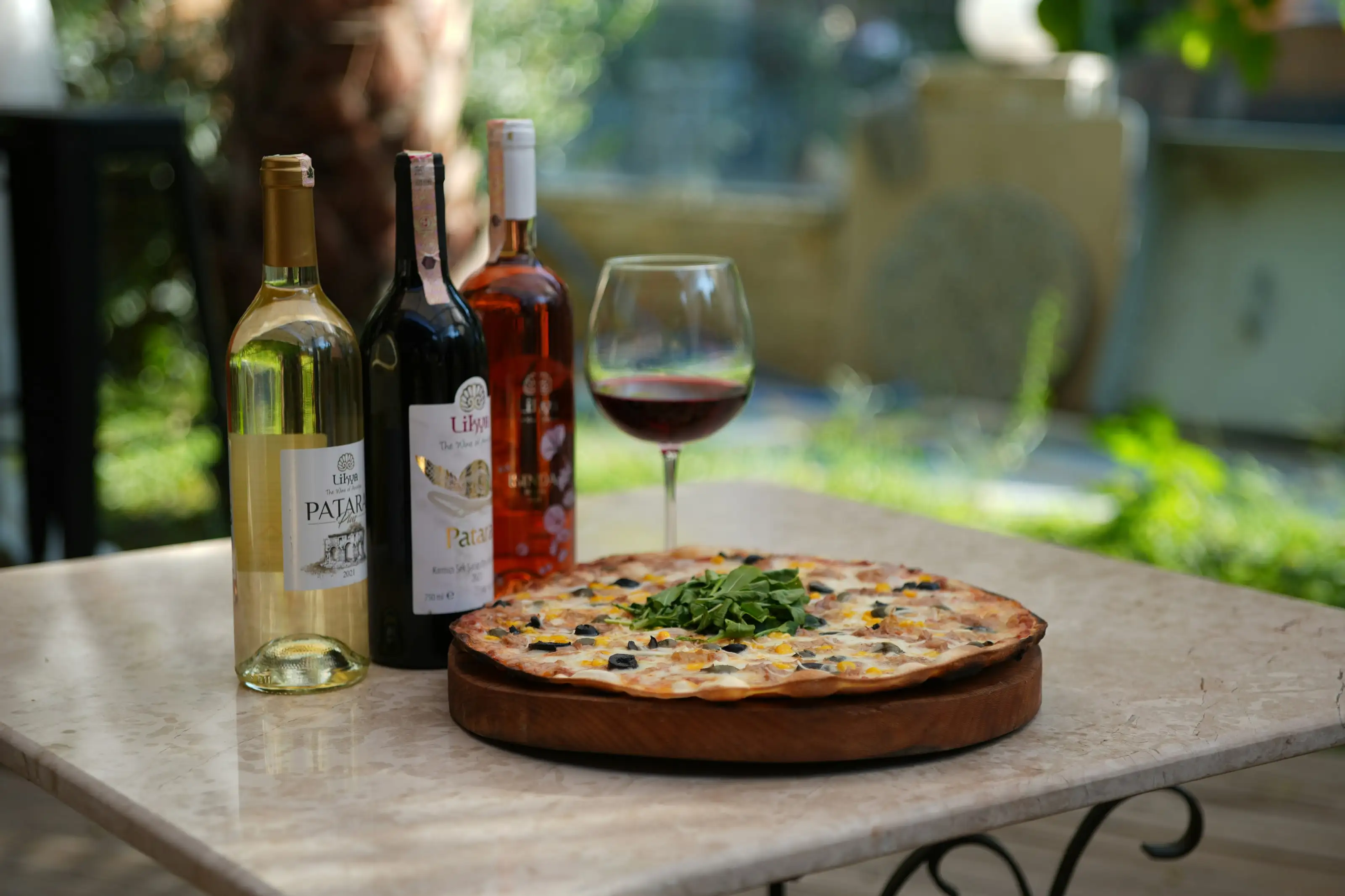 Weinflaschen, Gläser und eine Pizza auf einem Tisch im Freien